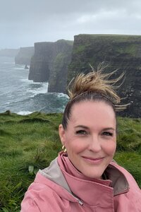 woman smiling at camera while standing on a cliff with wind blowing