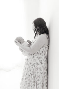 A black and white image of a mom looking down at her baby while holding him in her arms in a photography studio.