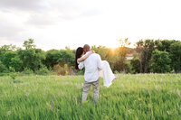 Couple with foreheads resting together, dressed in white, while holding her in his arms with sunset setting over the hill. Captured by Minnesota wedding photographer.