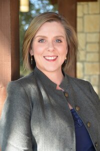 woman with short blonde hair smiling and wearing a gray blazer