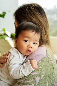 A baby boy rests against his mother's shoulder and gazes directly into the camera with big brown eyes during an at-home photo shoot in London.