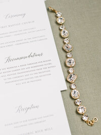 wedding invitations laid out on sage fabric and diamond braclet