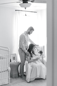 Black and white portrait through a doorframe of a lifestyle newborn session of mother and father holding their infant