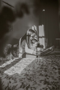 photo maman lit un livre a son petit garcon assis entre ses jambes sur le lit