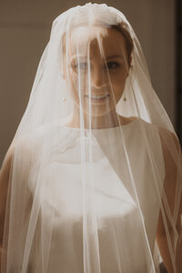 Radiant Minnesota bride smiles under the cover of her veil as the sunlight hits her face