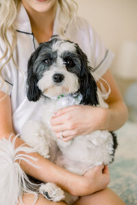 Bride in cozy PJs at Pensacola Beach, lovingly holding her dog before the wedding, sharing a tender, joyful moment with her furry companion.