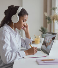 Young female creative business owner taking notes from a virtual group coaching call.
