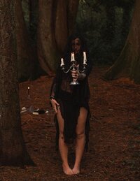 Woman dressed in gothic black veil holding candelabra in the forest