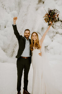 bride and groom smiling with hands up