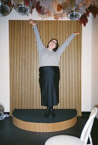 Woman standing under dried florals and disco balls holding her hands up in the air with excitement. Photo by Rhode Tripper Photography