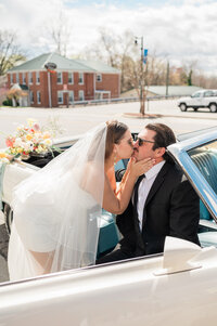 A person sitting in a convertible as their partner leans over and kisses them