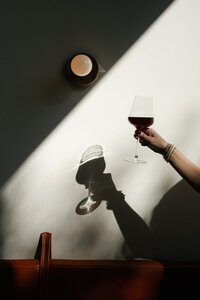 Hand holding a wine glass with the shadow reflecting on the wall behind it