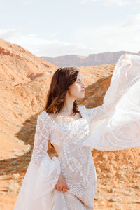 Elegant bride has her arm up with her dress blowing in the wind during a sunset elopement in Moab