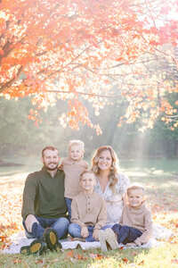 Family sitting, smiling at the camera at Wegerzyn Gardens in Dayton, Ohio on a bright fall morning.