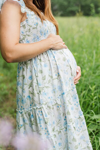 a mother holds her pregnant belly in an outdoor field