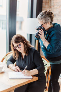 Amanda leans over the shoulder of a client, taking a picture of her working on planning content