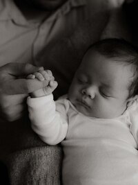 Close-up of a newborn’s tiny hand resting gently in a parent’s hand, in timeless black and white.