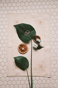 Wedding Flat Lay details film photography in Providence RI, Minimalist Wedding Detail photo on the tile bathroom floor and a creamy linen with two green leaves and a light blue ring box and dried oranges