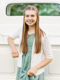 Girl smiling and standing by a white truck outside.