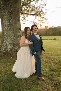 A bride is smiling while holding her new husband from behind at the barn in Virginia