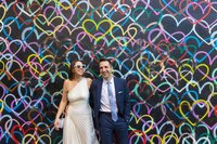 A wedding couple standing next to each other leaning up against a wall covered with a mural.