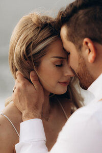 A close-up photo from a San Francisco photoshoot of a romantic couple intimately embracing, with a woman leaning her head gently against a man's forehead. Both are clad in light attire.