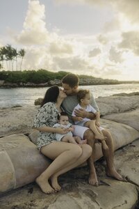 husband and wife share a kiss while holding their child on beach in south florida