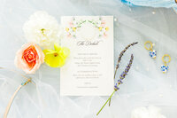 Wedding invitation laying on tulle surrounded by bright flowers