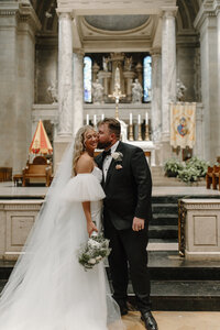 groom kissing bride's cheek in church