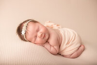 Newborn baby girl chin on hands pose studio pink backdrop with headband