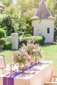 An ornately decorate table holds pink and purple floral arrangements.