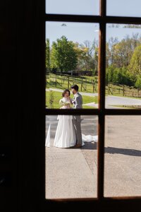 an artsy photo showing the view of a bride and groom through a window pane