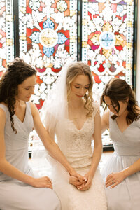 Catholic bride prays with her bridesmaids before her wedding ceremony Mass.