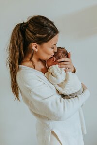 A woman holds and kisses a newborn baby.