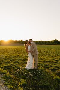 bride and groom kissing in a grassy field at sunset