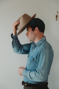 a man wearing vintage clothes putting on a cowboy hat