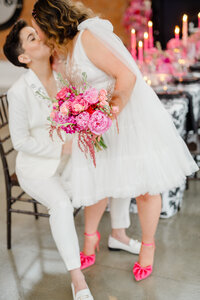Brides kissing off camera with pink wedding bouquet
