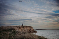 The photographer, Em, stands on a prairie bluff overlooking a lake at sunset.