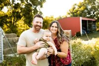 two parents smiling and standing next to each other while one holds a baby