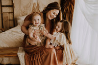 A mom and her two daughters sitting on a bed laughing in a boho photography studio in fort worth, texas