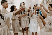 A bride holds up champagne and cheers with her bridesmaids