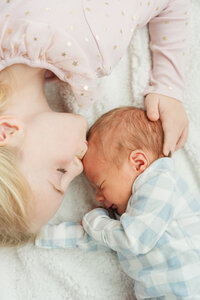 an older sister sibling kisses her newborn brother on the head while laying down