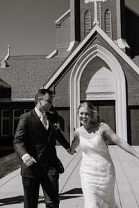 A couple holding hands and running outside a church