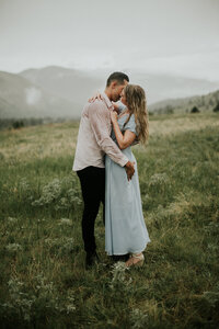 Couple kisses one another as their hands are wrapped around one another in a field as it rains