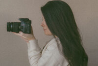 A photo of Michaela's profile as she is taking a photo with her camera. Her profile is almost fully covered by her hair.
