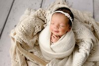 newborn girl with dark hair is swaddled in a boho styled ]][[basket in a charlotte area studio