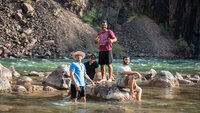 Group of men on a rock in shallow river.