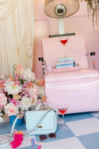 Styled salon flatlay featuring a pink retro dryer chair with stacked fashion books, a red cocktail, designer handbag, sunglasses, floral bouquet, and disco balls — editorial detail by Greenville South Carolina portrait photographer Dani Lacey Photographs.