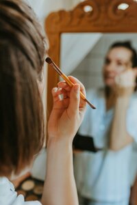 Reflection of a woman in a mirror applying makeup, representing makeup lessons from Looks with Libby.