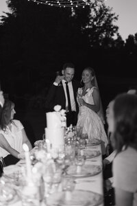 Black and white wedding photography in Rexburg Idaho. A bride and groom at their reception, looking at the wedding cake, smiling and laughing.